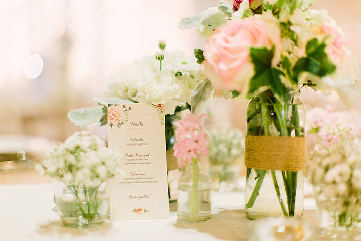 mesa de casamento com ementa design floral e flores rosa e branca com jarro de vidro e rafia
