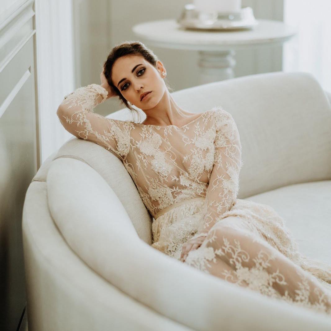noiva com vestido rendado transparente manga comprida sentada num sofá