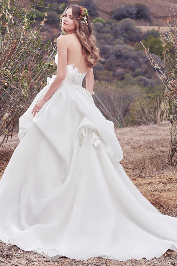Um vestido simples no entanto repleto de glamour com a sua organza Cameo. Apresenta pregas suaves no corpete e uma saia volumosa. Um decote em forma de coração exclusivo e pormenores florais 3D feitos à mão sao realçados com cristais Swarovski na cintura. Isto combinado com a saia originam um look bastante romântico. Terminado com um fecho.