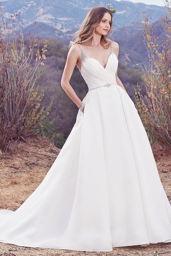 Este vestido de noiva Shavon Organza apresenta um corpete assimétrico e pregas suaves ao longo da saia. Alças deslizam directamente do decote em V até ao V também das costas. Um cinto com cristais Swarovski completa este look que exibe um romance único. Terminado com botões na área do fecho.