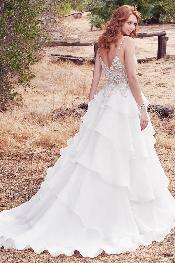 Este vestido de noiva maravilhoso apresenta um corpete de renda bordado decorado com cristas Swarovski e, ainda, alças finas, decote em forma de U e ilusão em forma de V nas costas. Uma saiade Celia organza assimétrica complete este look fabuloso. Terminado com botões de cristais na zona do fecho.