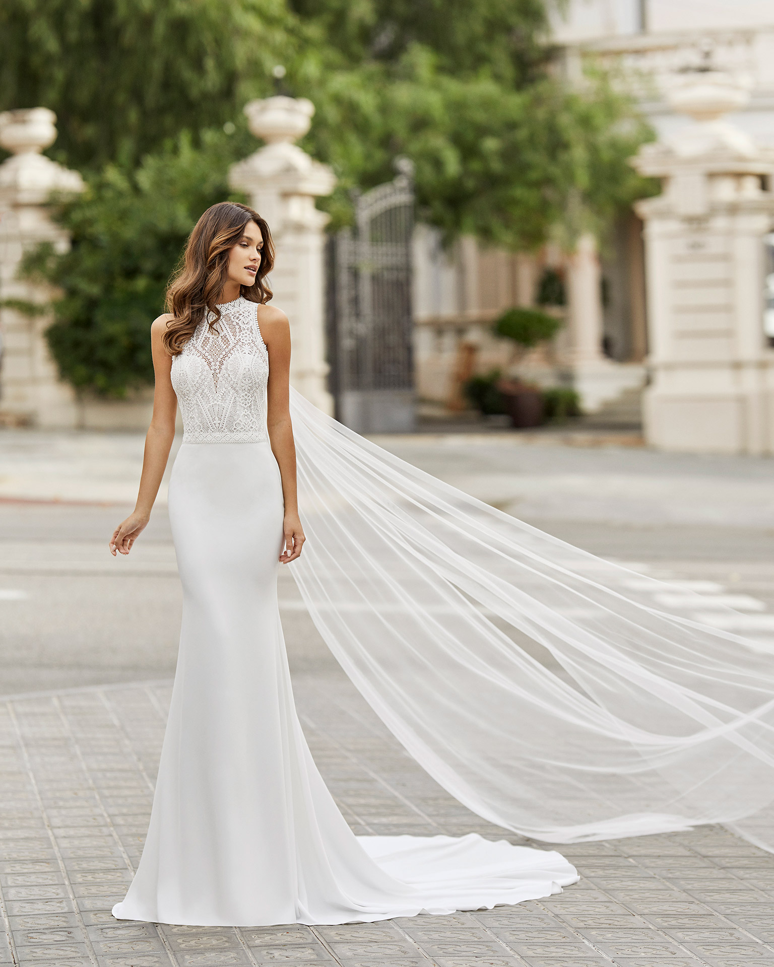 Leve, sexy e primaveril, o modelo Tamesis é ideal para um casamento civil, embora possua uma capa desmontável para um look mais recatado. De corte sereia, a terminar em cauda, exibe um corpete de renda, transparências, decote halter e costas abertas, que compensam a simplicidade da saia. | Rosa Clará 2021