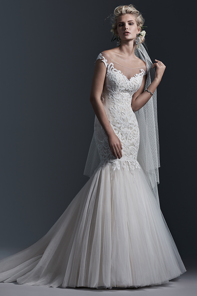 Uma renda com padrão arrojado constitui este vestido com decote ilusão e corte sereia. Terminado com botões em vez de um fecho.
<a href="https://www.maggiesottero.com/sottero-and-midgley/cassandra/9362" target="_blank">Sottero and Midgley</a>