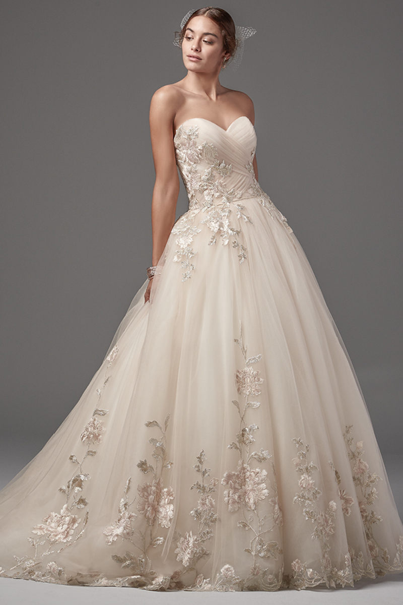 Um bordado blush e rendas douradas caem em cascata ao longo do tule neste magnífico vestido com efeito balão sem alças, apresentando um corpete com pregas e um decote em forma de coração. Terminado com botões de cristas em vez de um fecho e um espartilho interior.
<a href="https://www.maggiesottero.com/sottero-and-midgley/decadence/10215?utm_source=mywedding.com&utm_campaign=spring17&utm_medium=gallery" target="_blank">Sottero and Midgley</a>