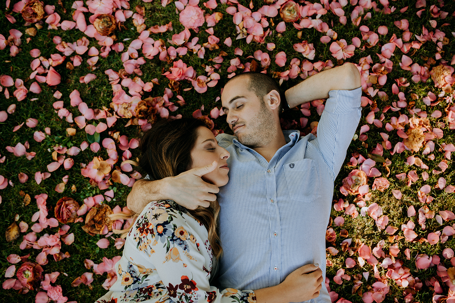 casal abraçado sobre cama de relva de pétalas de flores 