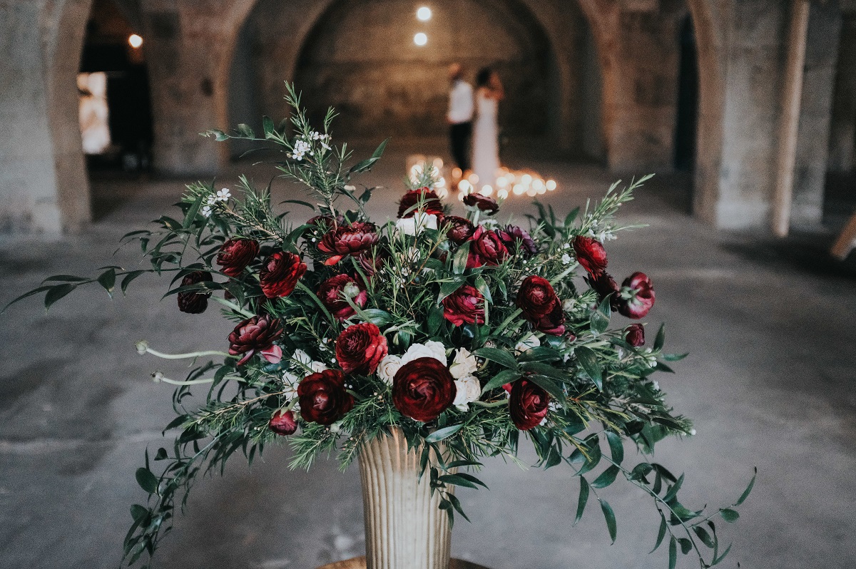 vaso com folhagens e rosas vermelhas noivos ao longe com velas