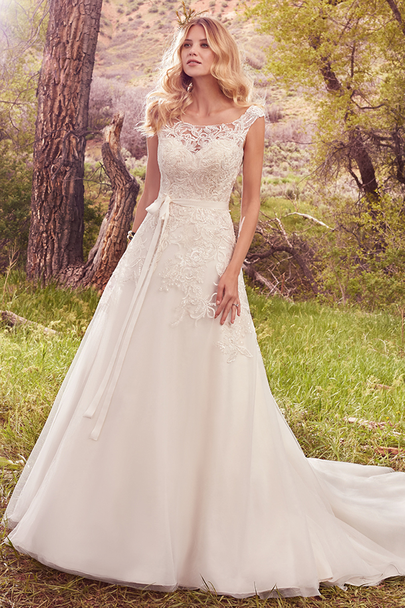 Embroidered lace appliqués cascade over the bodice, illusion sweetheart neckline, and illusion cap-sleeves of this gorgeous A-line, featuring a keyhole back and tulle skirt. Finished with covered buttons over zipper closure. Style includes grosgrain ribbon belt. 
<a href="https://www.maggiesottero.com/maggie-sottero/ophelia/10129?utm_source=mywedding.com&amp;utm_campaign=spring17&amp;utm_medium=gallery" target="_blank">Maggie Sottero</a>