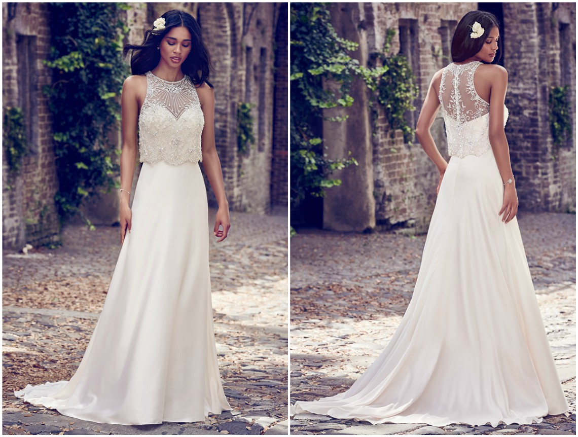 Uma jaqueta transparente destacável, adornada com pedraria e cristais Swarovski, cobre o corpete de decote coração deste vestido em cetim, de inspiração vintage e corte linha A. Acabamentos com botões de cristal sobre fecho zíper. <a href="https://www.maggiesottero.com/maggie-sottero/larkin/11176?utm_source=zankyou&utm_medium=gowngallery" target="_blank">Maggie Sottero</a>