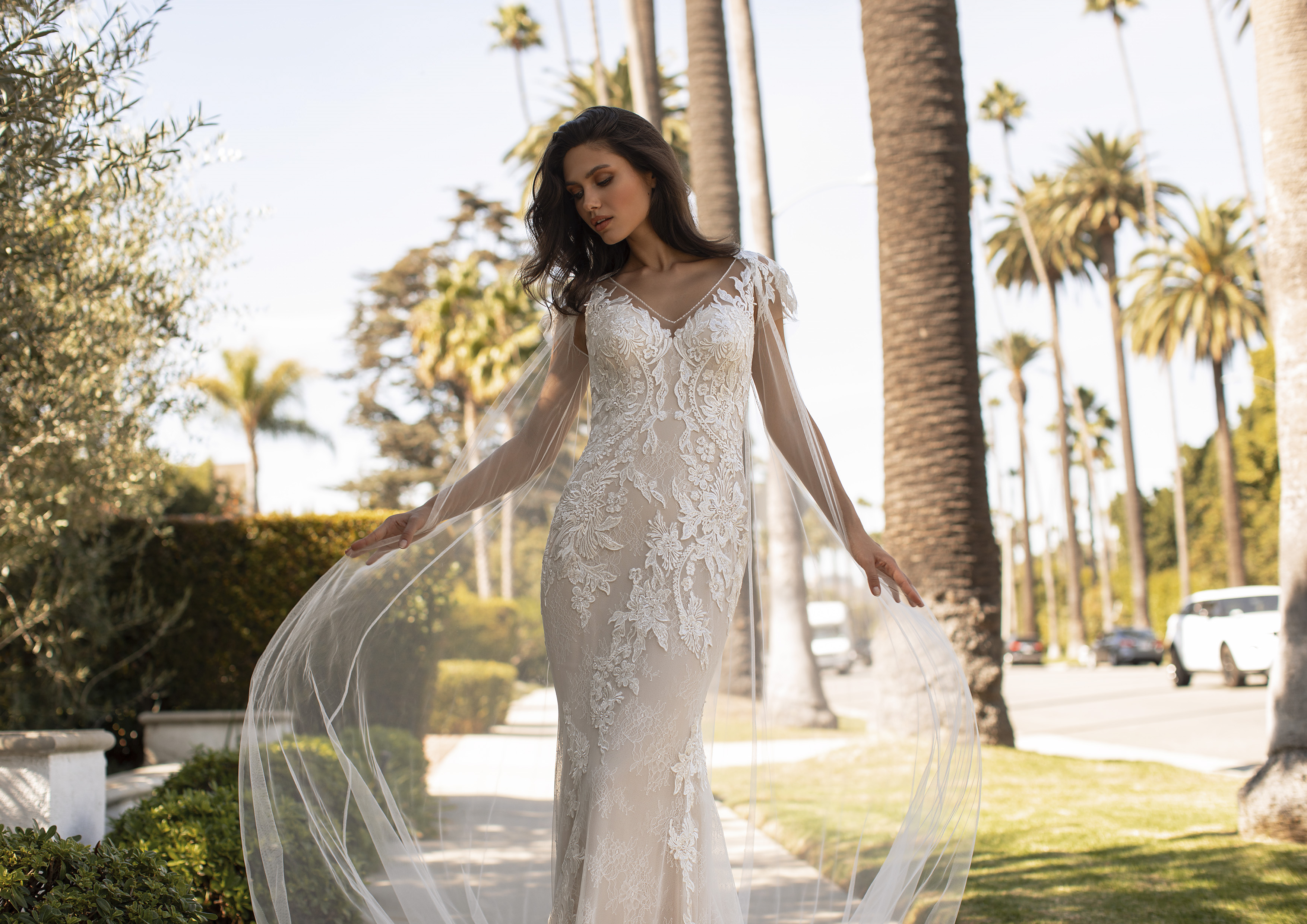 Vestido de bainha semitransparente, com uma leve cauda real, sedutoras costas keyhole e pedraria artesanal nos ombros, braços e decote em bico | Modelo Dehaven da Pronovias 2021 Cruise Collection – Ashley Graham X Pronovias