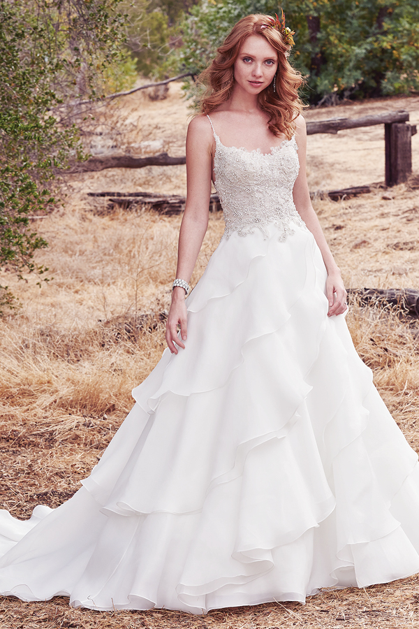 Este vestido de noiva maravilhoso apresenta um corpete de renda bordado decorado com cristas Swarovski e, ainda, alças finas, decote em forma de U e ilusão em forma de V nas costas. Uma saiade Celia organza assimétrica complete este look fabuloso. Terminado com botões de cristais na zona do fecho.
