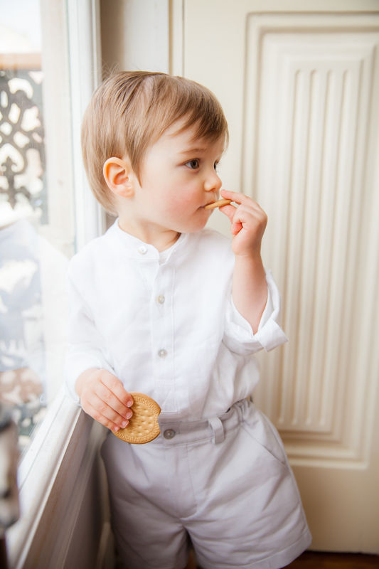 menino com calção e camisa cores neutras a comer uma bolacha