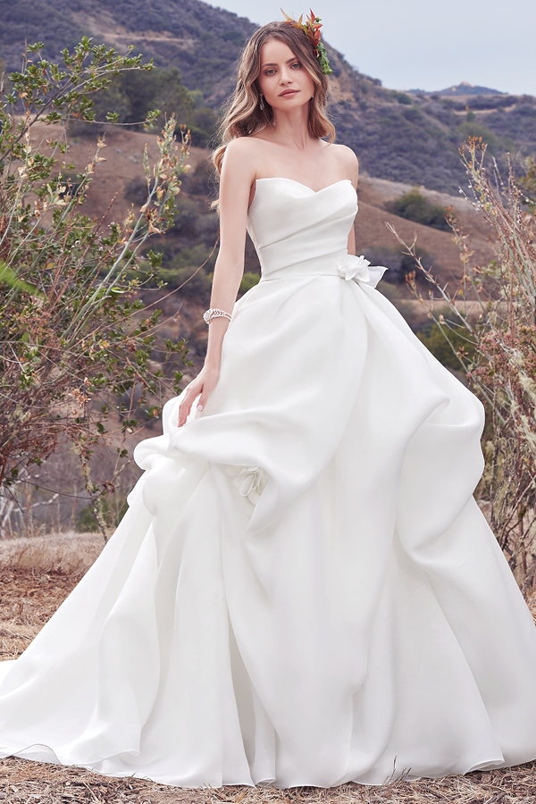 Um vestido simples no entanto repleto de glamour com a sua organza Cameo. Apresenta pregas suaves no corpete e uma saia volumosa. Um decote em forma de coração exclusivo e pormenores florais 3D feitos à mão sao realçados com cristais Swarovski na cintura. Isto combinado com a saia originam um look bastante romântico. Terminado com um fecho.