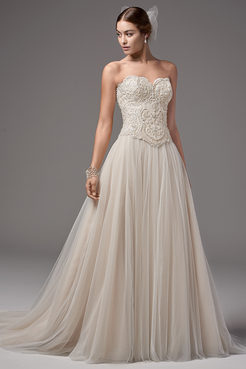 Este corpete apresenta um decote em forma de coração e magnificentes detalhes em renda embelezados com pérolas, contas e cristais Swarovski. Terminado com botões em vez do fecho. Um elegante tule Linha-A constitui a saia que realça a linha natural da cintura. Terminado com fecho.
<a href="https://www.maggiesottero.com/sottero-and-midgley/carrington---shardea/10300?utm_source=mywedding&utm_campaign=spring2017&utm_medium=gallery" target="_blank">Sottero and Midgley</a>