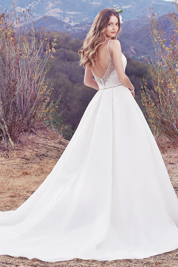 Este vestido de noiva Shavon Organza apresenta um corpete assimétrico e pregas suaves ao longo da saia. Alças deslizam directamente do decote em V até ao V também das costas. Um cinto com cristais Swarovski completa este look que exibe um romance único. Terminado com botões na área do fecho.
