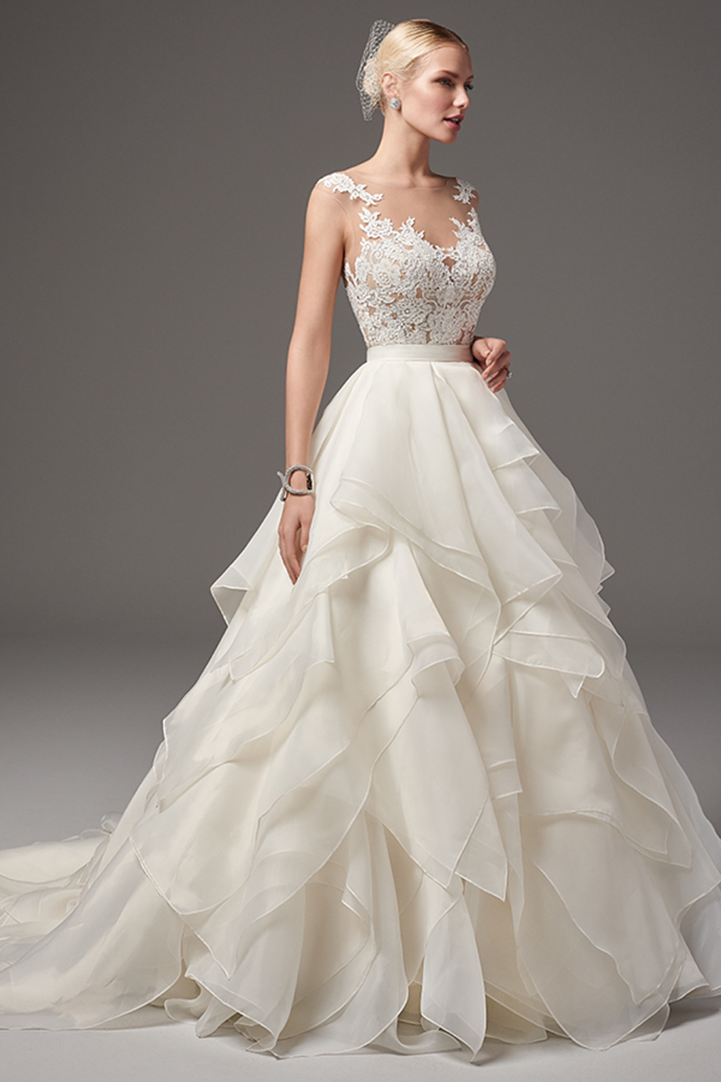 This sexy and romantic bodysuit features scattered lace appliqués over an illusion sweetheart neckline, illusion cap-sleeves, and illusion open back. Finished with crystal button closure. Layered Marquice organza ballgown skirt with zipper closure.
<a href="https://www.maggiesottero.com/sottero-and-midgley/tristan---gemma/10298?utm_source=mywedding&utm_campaign=spring2017&utm_medium=gallery" target="_blank">Sottero and Midgley</a>
