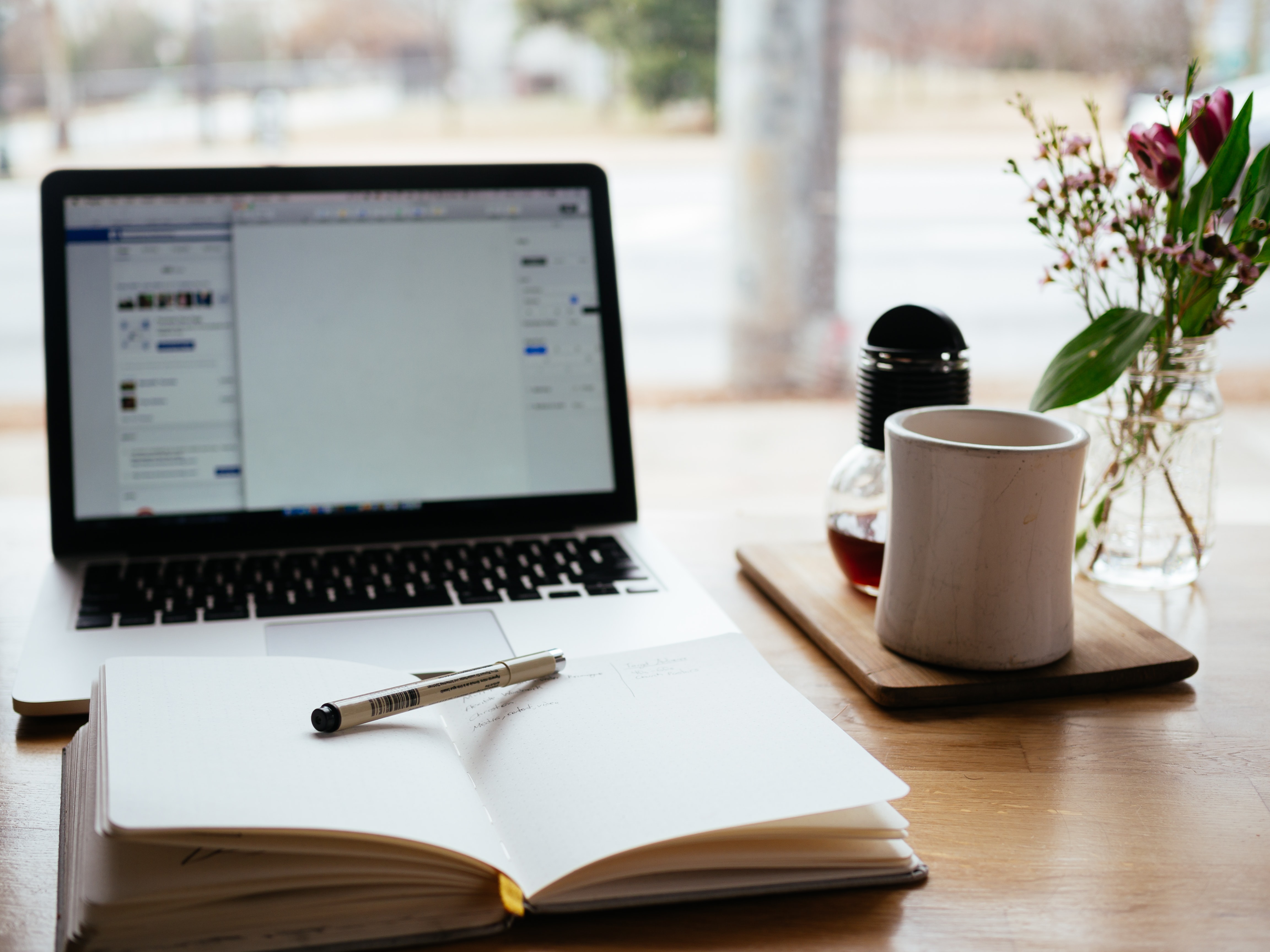 mesa com computador e agenda e chávena de café