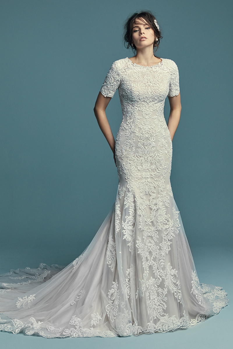 <a href="https://www.maggiesottero.com/maggie-sottero/della-marie/11467">Maggie Sottero</a>
Pormenores de renda dançam ao longo do tule que constitui este vestido de noiva fit-and-flare. Complementado com um gola com joias e mangas pelos cotovelos. Terminado com botões cobertos sobre um fecho.