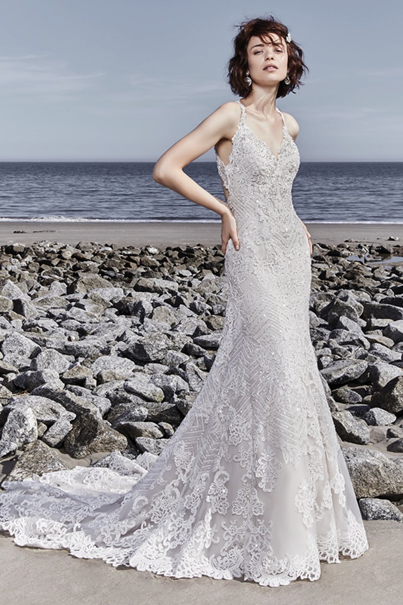 Este vestido de noiva único apresenta detalhes de renda chique espalhados entre cristais Swarovski e pormenores geométricos. As alças decoradas com renda deslizam do decote em V até às costas sexy. Termina com botões que cobrem o fecho.
<a href="https://www.maggiesottero.com/sottero-and-midgley/holden/11540">Sottero and Midgley</a>