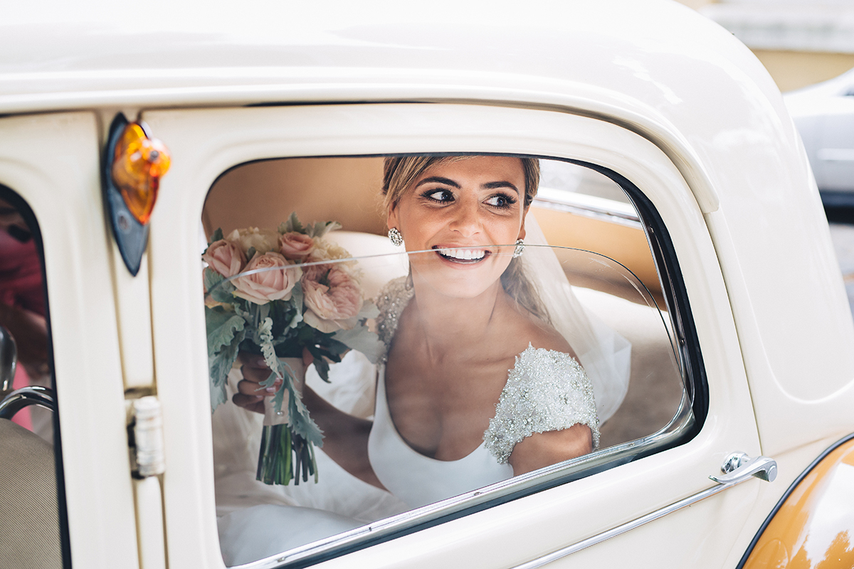 noiva a sorrir dentro do carro com bouquet na mão