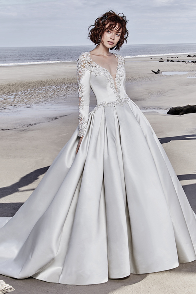 Este vestido de noiva Carlo Satin de cortar a respiração apresenta mangas compridas, confecionadas com detalhes e bordados de renda. Cristais Swarovski decoram a linha da cintura que dá lugar a uma saia volumosa e plissada com bolsos. Um vestido complementado com um decote em V e as costas em forma de U. .
<a href="https://www.maggiesottero.com/sottero-and-midgley/brennon/11523">Sottero and Midgley</a>